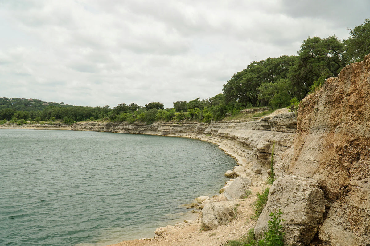 A quiet Texas Hill Country lake curves between pale limestone bluffs.