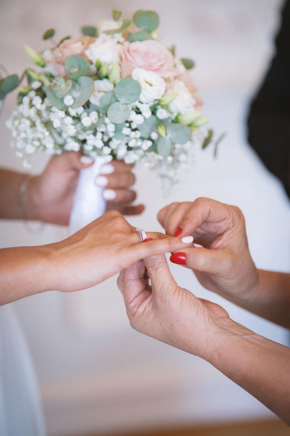 Close hands exchange a wedding ring beside a soft white bouquet.