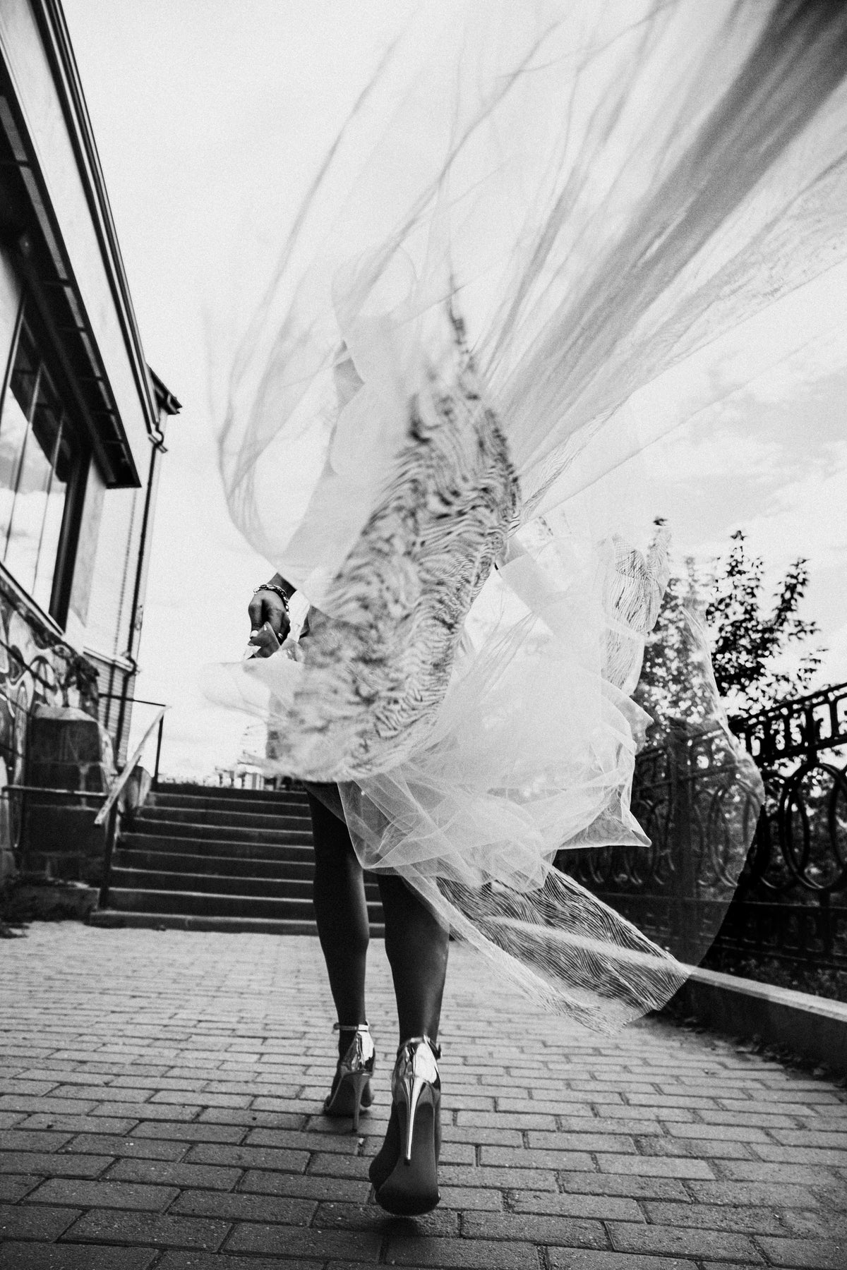 A bride moves up an outdoor staircase as her veil catches the air.