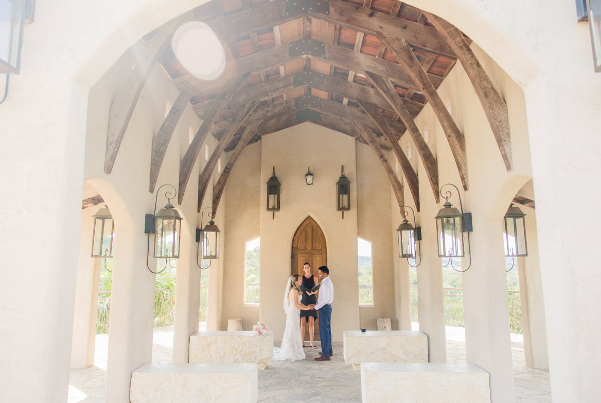 A couple framed by the light-filled arches of an open-air chapel.