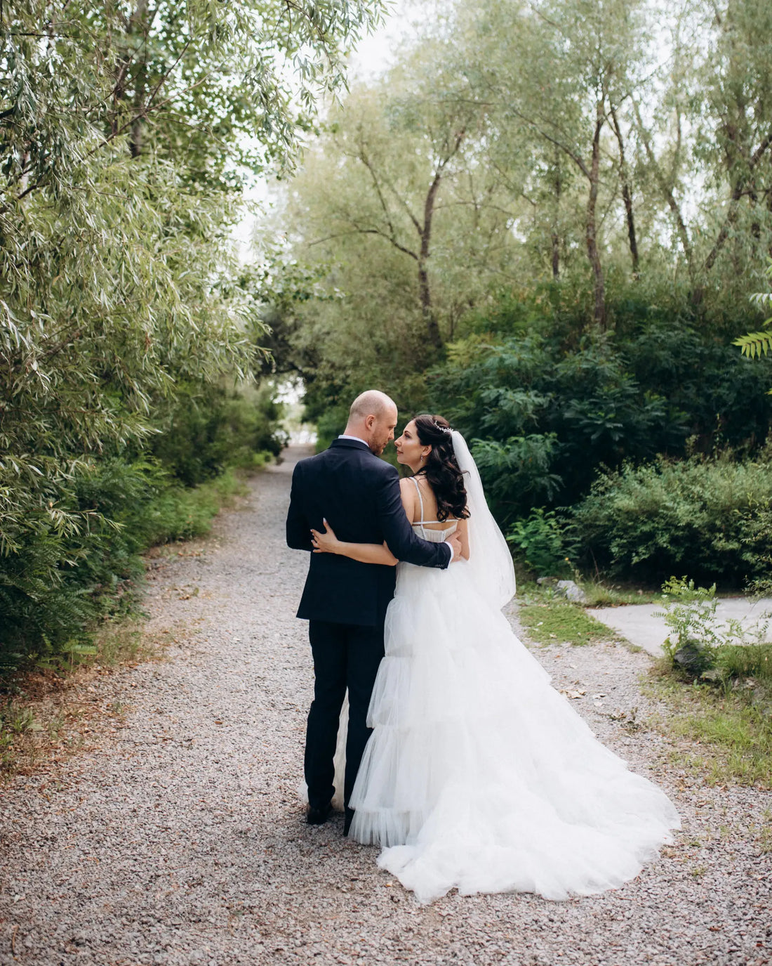 A newlywed couple walking together through a lush garden.