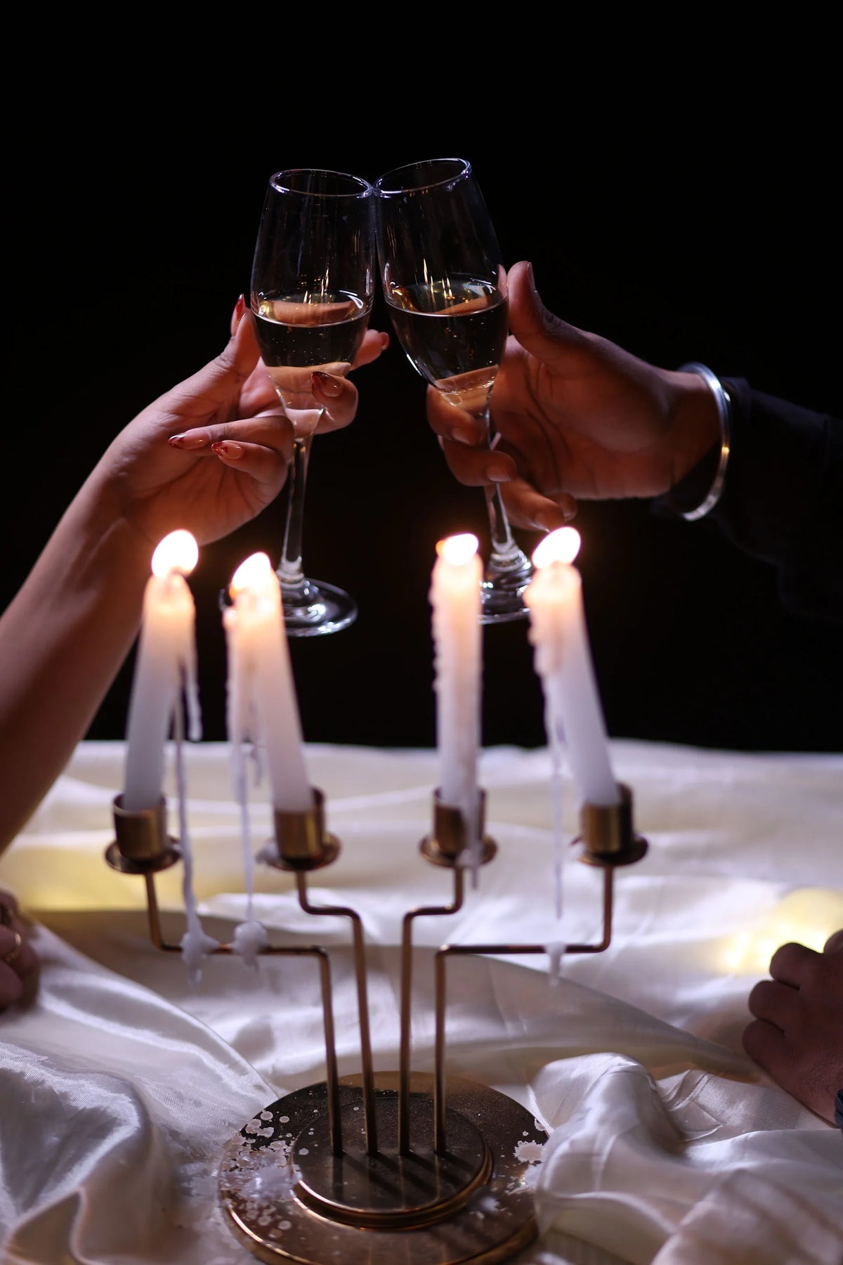 Two hands toast champagne above a candlelit dinner table.