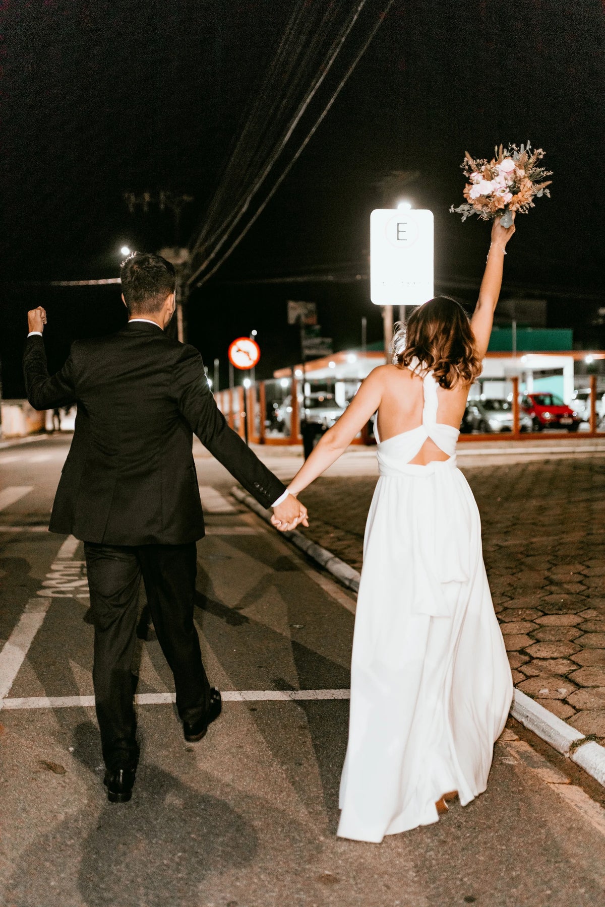 Newlyweds hold hands during a celebratory walk through a city at night.