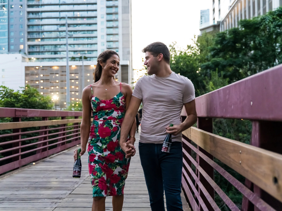 A couple walks hand in hand on an Austin city bridge during the day.