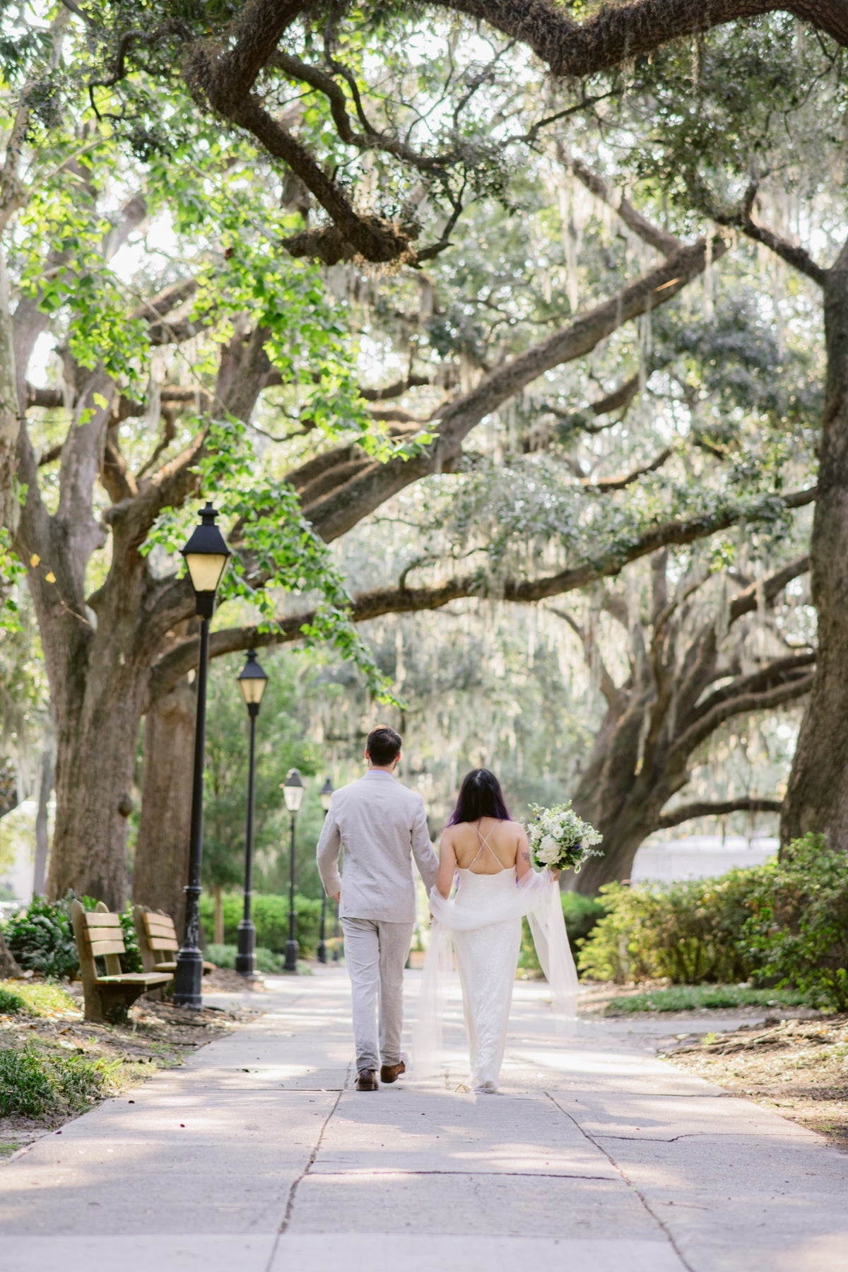 A couple walking beneath live oaks and Spanish moss in Forsyth Park. Josh Stewart Photography.