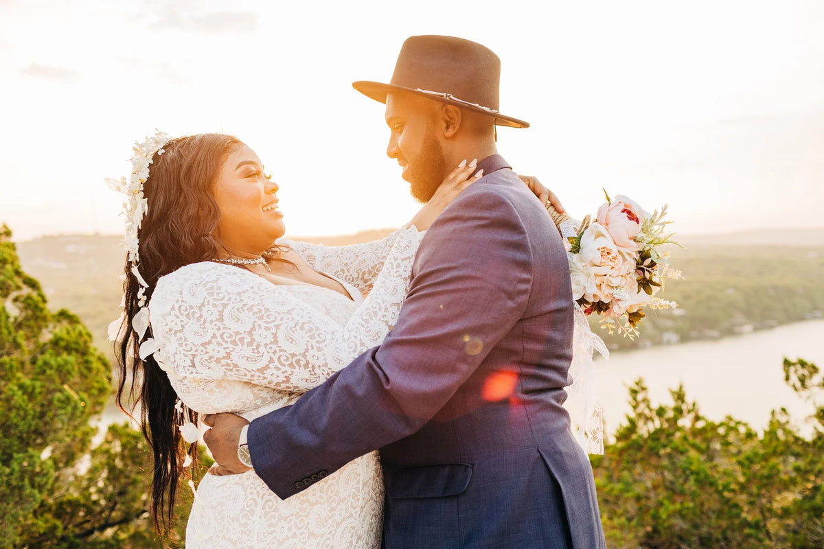 Newlyweds share an embrace beside a lake in warm evening light.